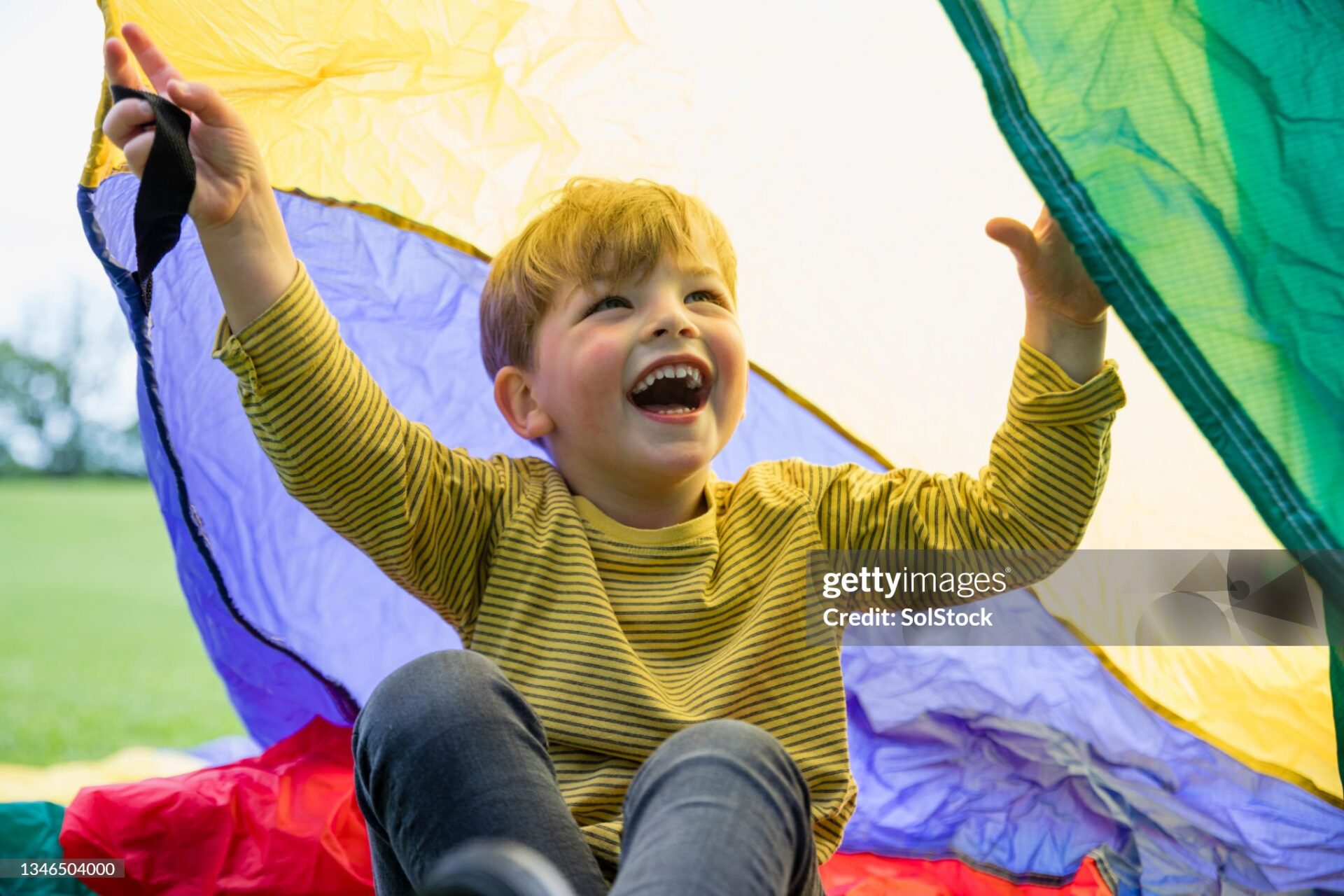 Young boy at preschool playing with a parachute in the North East of England.